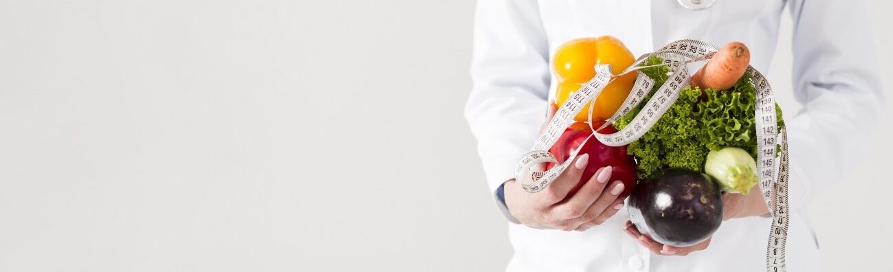 Woman holds lettuce, red and yellow chili, carrot, leek and an eggplant in hands that are surrounded by a measuring tape